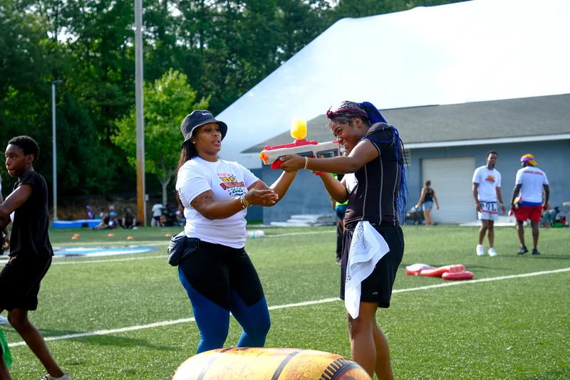 A coach and a child play a foam-baton balance game on the field