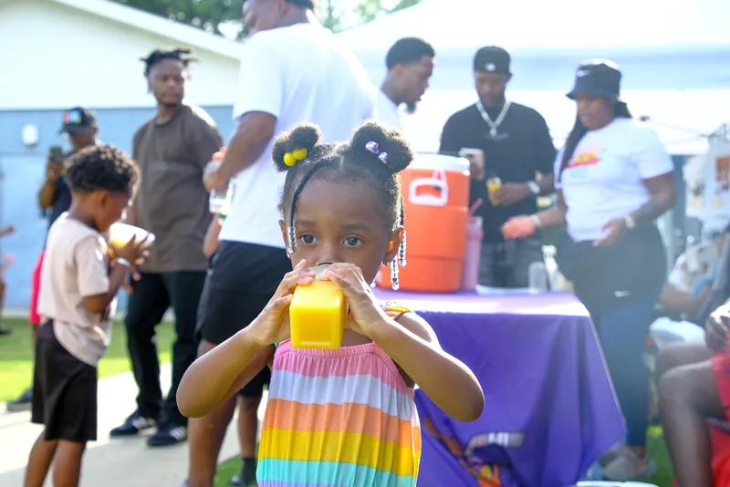 A young girl in a rainbow dress sips a drink at the hydration table
