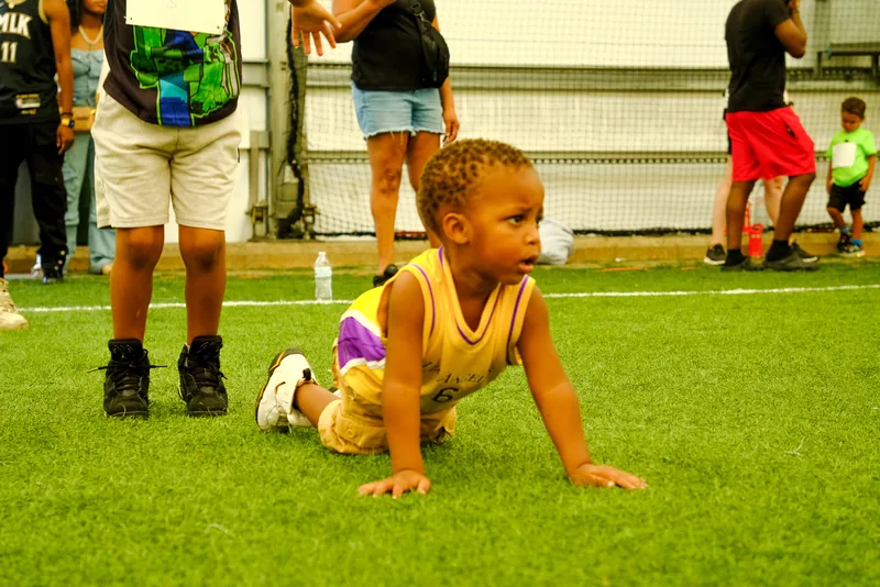 A toddler in a jersey bear-crawls across the turf during a Faith First Fitness session